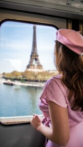 Frau mit rosa Kleid und rosa Mütze schaut durch ein Fenster auf den Eiffelturm, Paris
