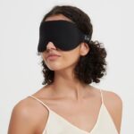 Frau trägt eine schwarze Schlafmaske aus Memory Foam, seitliche Ansicht mit elegantem Look.