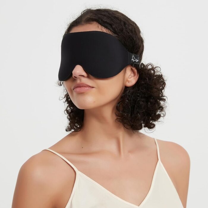 Frau trägt eine schwarze Schlafmaske aus Memory Foam, seitliche Ansicht mit elegantem Look.