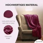 Eine weiche, dunkelrote Decke aus hochwertigem Material liegt über einem braunen Sessel. Links im Bild sind Nahaufnahmen der verstärkten Nähte und des flauschigen Stoffs zu sehen. Der Text hebt die Qualität und Wärme der Decke hervor.