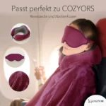 Schlafmaske und Ohrstöpsel für entspanntes Reisen. Eine Person schläft im Flugzeug mit einer dunkelroten Schlafmaske, einem Nackenkissen und einer weichen Reisedecke. Kleine Kreise zeigen Nahaufnahmen der Materialien und des Zubehörs.