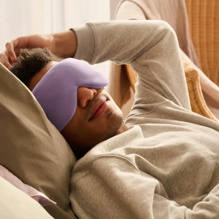 Ein Mann liegt entspannt auf einem Bett und trägt eine gewichtete Schlafmaske in Lavendelfarbe. Die weiche Maske passt sich sanft seinem Gesicht an und sorgt für eine beruhigende Schlafumgebung. Die gemütliche Atmosphäre im Raum unterstreicht das Gefühl von Entspannung und Erholung.