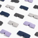 Mehrere gewichtete Schlafmasken in verschiedenen Farben, darunter Lavendel, Grau, Marineblau und Beige, sind auf einer weissen Oberfläche angeordnet. Die ergonomische Form und das weiche Material der Masken sind deutlich zu erkennen und vermitteln Komfort und Entspannung.