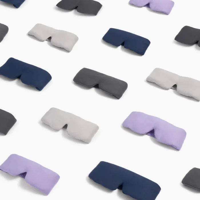 Mehrere gewichtete Schlafmasken in verschiedenen Farben, darunter Lavendel, Grau, Marineblau und Beige, sind auf einer weissen Oberfläche angeordnet. Die ergonomische Form und das weiche Material der Masken sind deutlich zu erkennen und vermitteln Komfort und Entspannung.