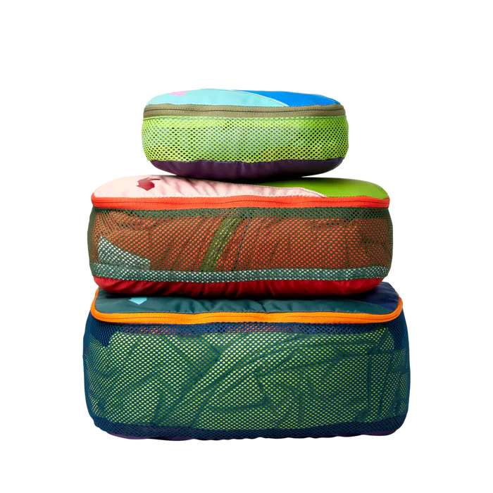 Drei Cotopaxi-Packwürfel in verschiedenen Grössen (2L, 3L, 10L) übereinandergestapelt, aus bunten Stoffresten gefertigt, mit Mesh-Einsätzen für Belüftung.