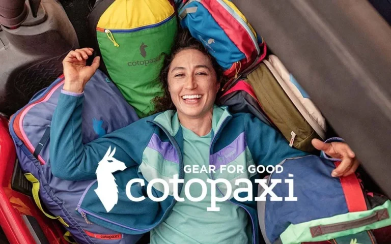 Lächelnde Frau liegt entspannt zwischen bunten Cotopaxi-Taschen, umgeben von farbenfroher Outdoor-Ausrüstung; im Vordergrund das Cotopaxi-Logo mit dem Slogan ‚Gear for Good