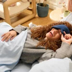 Frau mit Schlafmaske liegt entspannt im Bett und lächelt