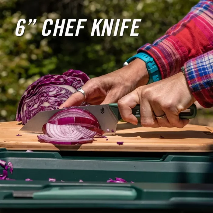 Person schneidet mit einem Camping Messer rote Zwiebeln auf einem Holzbrett, im Hintergrund liegt ein halbierter Rotkohl.