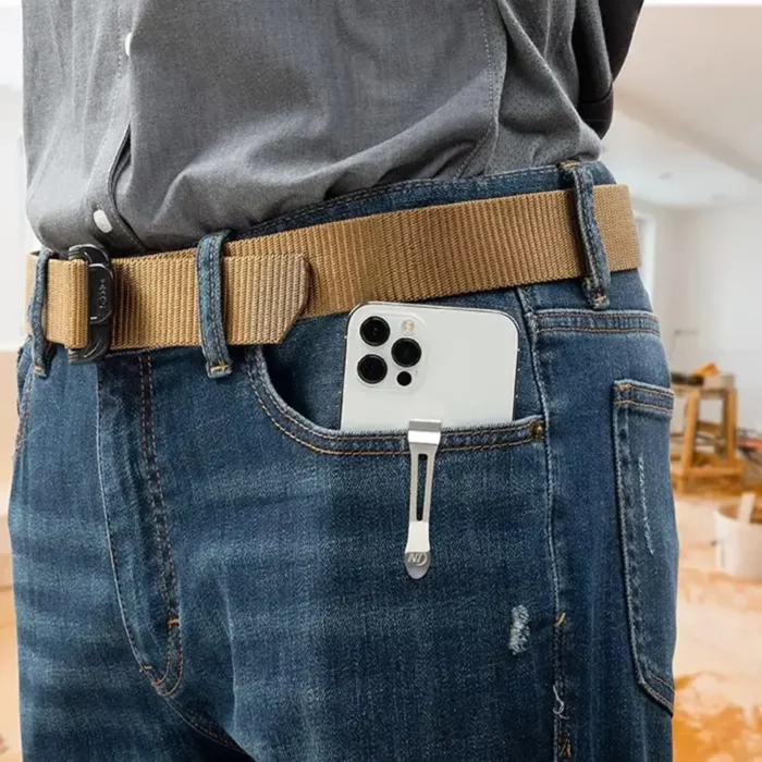 Smartphone mit einem Gürtelclip an der Hosentasche einer Jeans befestigt, darüber ein brauner Gürtel und graues Hemd.