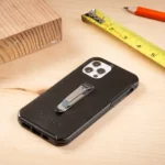 Smartphone mit schwarzer Hülle und montiertem Gürtelclip liegt auf einem Holztisch, daneben ein Zollstock, ein Bleistift und ein Stück Holz.