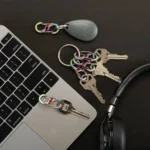 Mehrere Schlüssel und ein Schlüsselanhänger mit Regenbogenfarben-Karabiner Schlüsselanhängern liegen auf einem schwarzen Tisch neben einem Laptop und einem Kopfhörer.