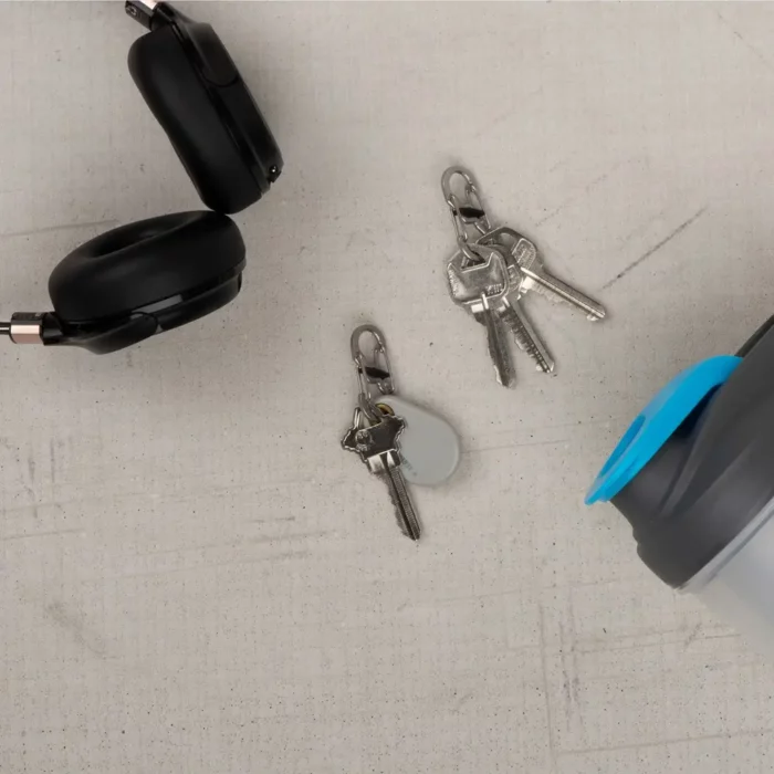 Zwei Karabiner Schlüsselanhänger mit daran befestigten Schlüsseln liegen auf hellem Untergrund neben schwarzen Kopfhörern und einer Trinkflasche mit blauem Deckel.