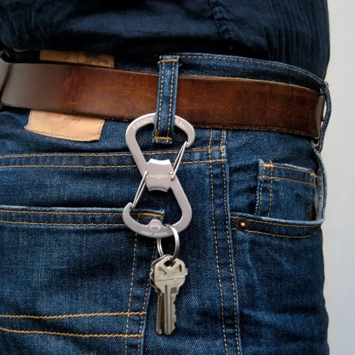 Flaschenöffner Schlüsselanhänger in Silber mit einem Schlüsselbund an einer Gürtelschlaufe einer Jeans befestigt, getragen mit braunem Ledergürtel.