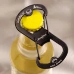 Schwarzer Flaschenöffner Schlüsselanhänger in Karabinerform wird an einem gelben Kronkorken einer Glasflasche angesetzt.