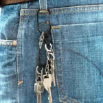 Schlüssel Karabiner mit mehreren daran befestigten Schlüsseln hängt an einer Gürtelschlaufe einer blauen Jeans neben einem braunen Ledergürtel.