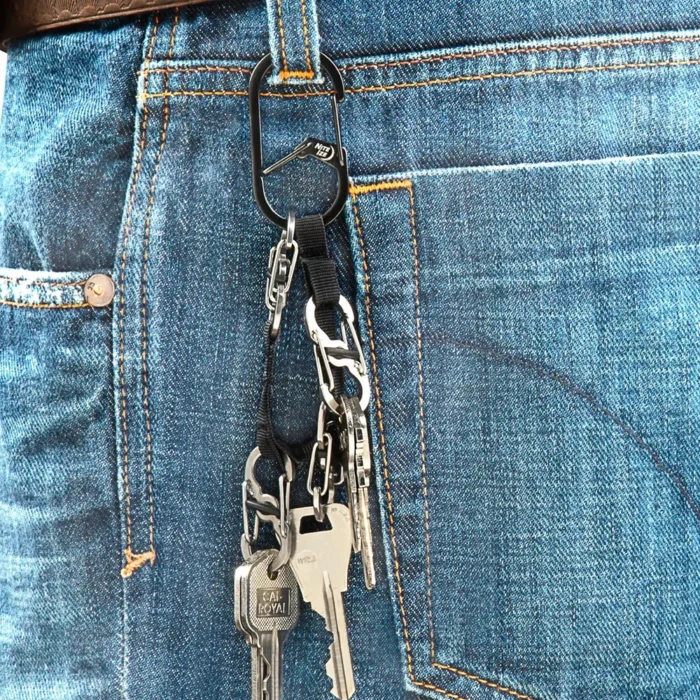 Schlüssel Karabiner mit mehreren daran befestigten Schlüsseln hängt an einer Gürtelschlaufe einer blauen Jeans neben einem braunen Ledergürtel.