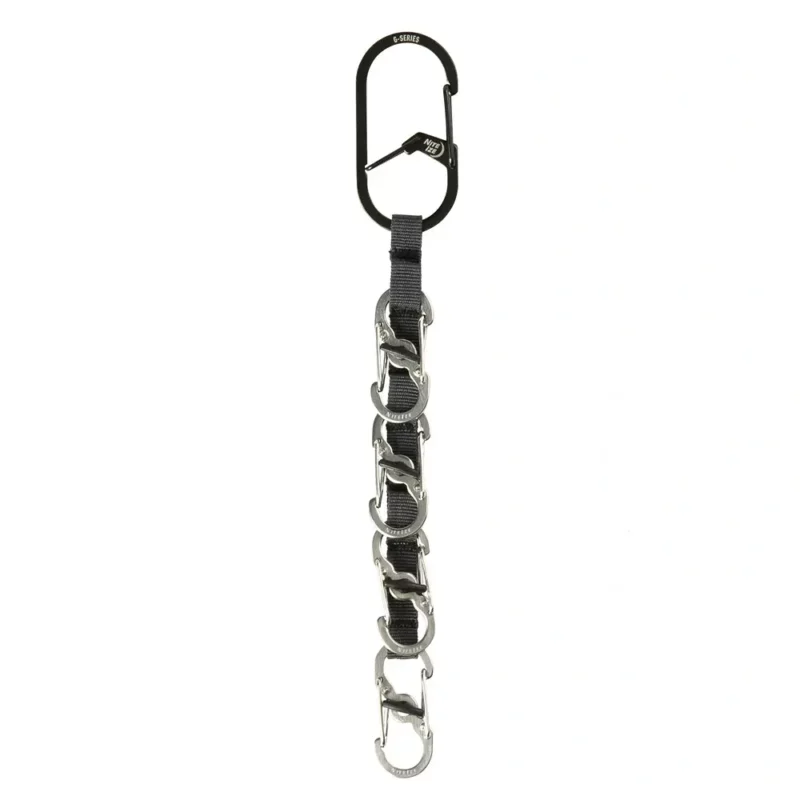 Schlüssel Karabiner mit schwarzem Hauptkarabiner und fünf kleinen silbernen Karabinern an einem schwarzen Gurtband vor weissem Hintergrund.