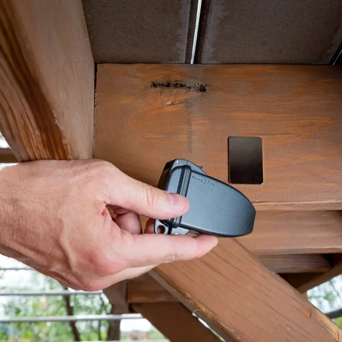 Eine Hand bringt eine schwarze Schlüsselbox Auto unter einem Holzdeck an, in der Nähe einer Metallplatte zur sicheren Befestigung.