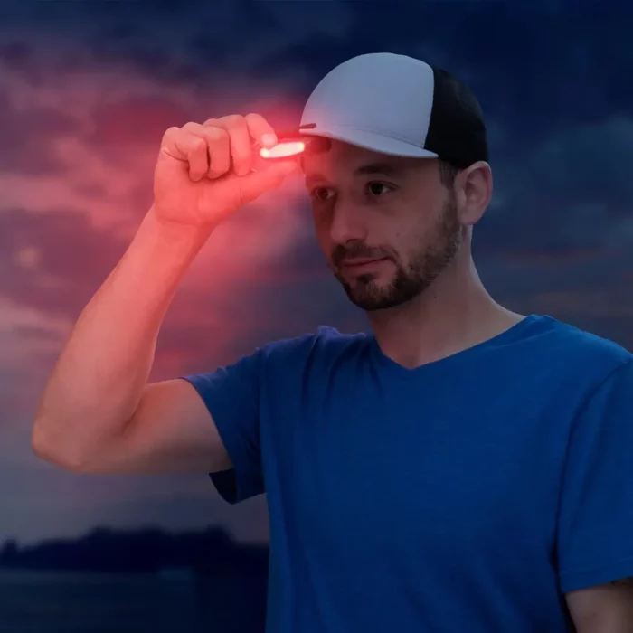 Mann mit Baseballcap und blauem T-Shirt hält eine kleine Clip Lampe mit rotem Licht an den Schirm seiner Kappe, im Hintergrund eine dunkle Abendstimmung.