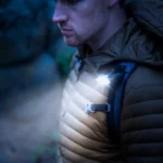 Ein Mann trägt eine leuchtende Clip Lampe, die an seinem Rucksackträger befestigt ist, bei Dämmerung oder Dunkelheit in einer Outdoor-Umgebung.