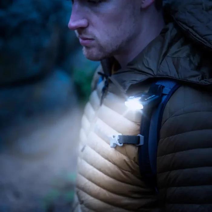 Ein Mann trägt eine leuchtende Clip Lampe, die an seinem Rucksackträger befestigt ist, bei Dämmerung oder Dunkelheit in einer Outdoor-Umgebung.
