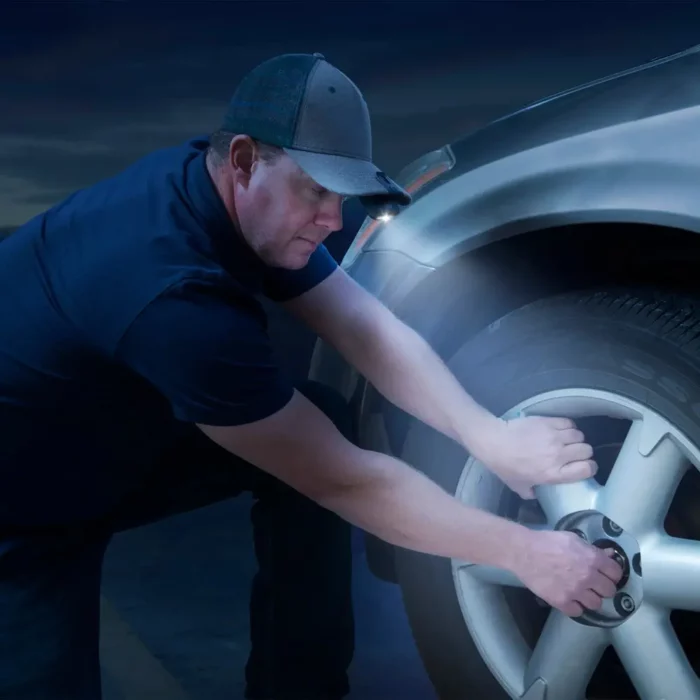 Ein Mann wechselt nachts ein Autoreifen und nutzt eine an seiner Cap befestigte Clip Lampe zur Ausleuchtung der Arbeit.