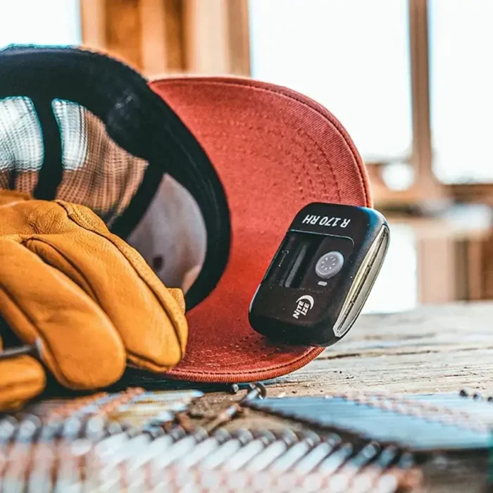 Nahaufnahme einer roten Cap mit befestigter Clip Lampe von Nite Ize, daneben Arbeitshandschuhe und Nägel – Szene auf einer Baustelle.