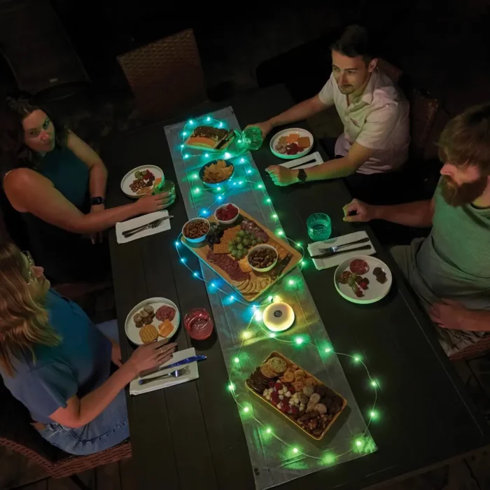 Gruppe von Freunden geniesst ein Abendessen im Freien, der Tisch ist stimmungsvoll mit einer grünen LED-Lichterkette dekoriert.