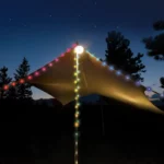Bunte LED-Lichterkette, gespannt über ein Zelt im Wald bei Nacht, mit Farben wie Rot, Blau, Gelb, Grün und Lila – stimmungsvolle Beleuchtung unter Sternenhimmel.