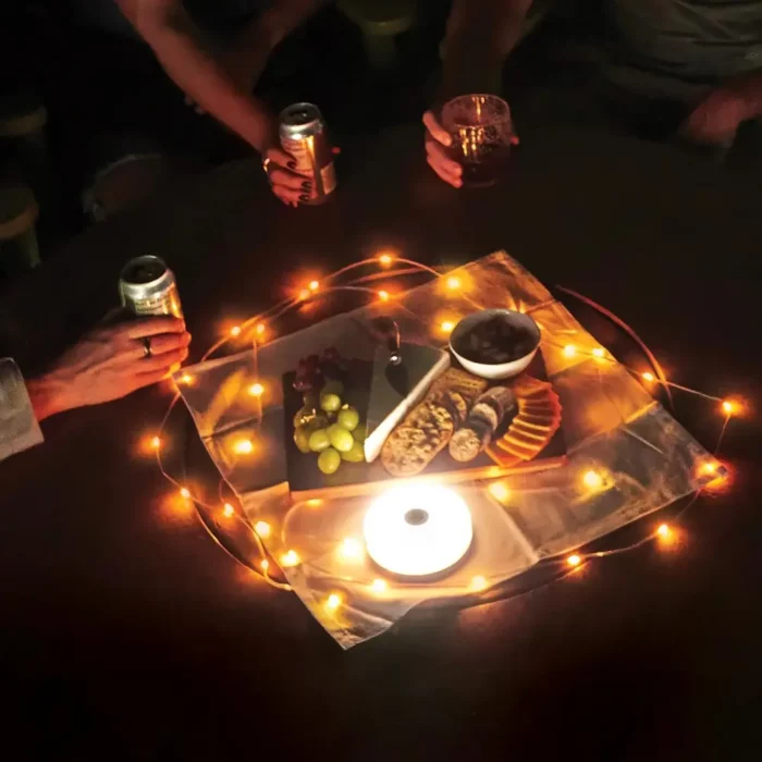 Warme LED-Lichterkette leuchtet auf einem Tisch bei Nacht, dekoriert mit Snacks, Käse, Trauben und Getränken – gemütliche Outdoor-Atmosphäre mit Freunden.