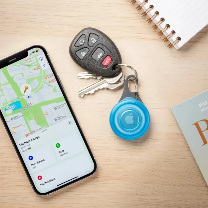 Ein Schlüsselbund mit integriertem Apple AirTag in einer Hunde Tracker Halterung liegt neben einem Smartphone, auf dem die Tracking-App geöffnet ist.