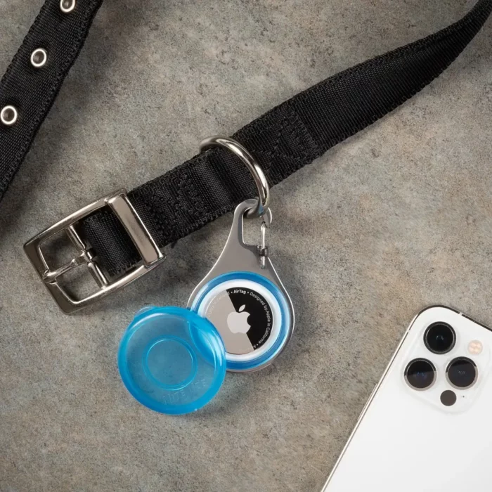 Die Hunde Tracker Halterung mit AirTag ist an einem schwarzen Halsband befestigt; daneben liegt ein Smartphone.