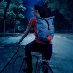 Eine Radfahrerin trägt einen Rucksack mit einem aktivierten roten Reflektor, der im Dunkeln gut sichtbar ist.