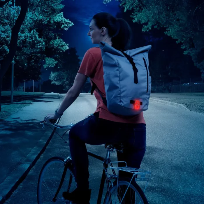 Eine Radfahrerin trägt einen Rucksack mit einem aktivierten roten Reflektor, der im Dunkeln gut sichtbar ist.