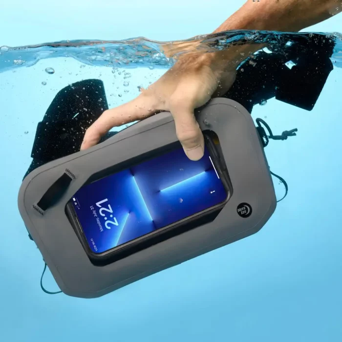 Eine Hand hält eine wasserdichte Gürteltasche unter Wasser – das Smartphone im Sichtfenster bleibt vollständig trocken und lesbar.