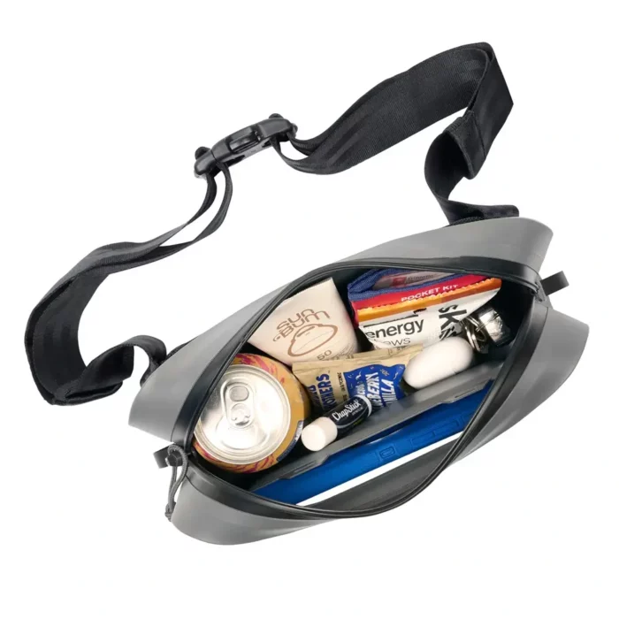 Die wasserdichte Gürteltasche ist geöffnet und zeigt ihren Inhalt – darunter Sonnencreme, Snacks, Getränkedose und weitere Utensilien für unterwegs.