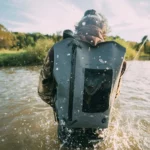 Eine Person watet durch einen Fluss, während ein wasserdichter Rucksack auf dem Rücken zuverlässig vor eindringendem Wasser schützt.