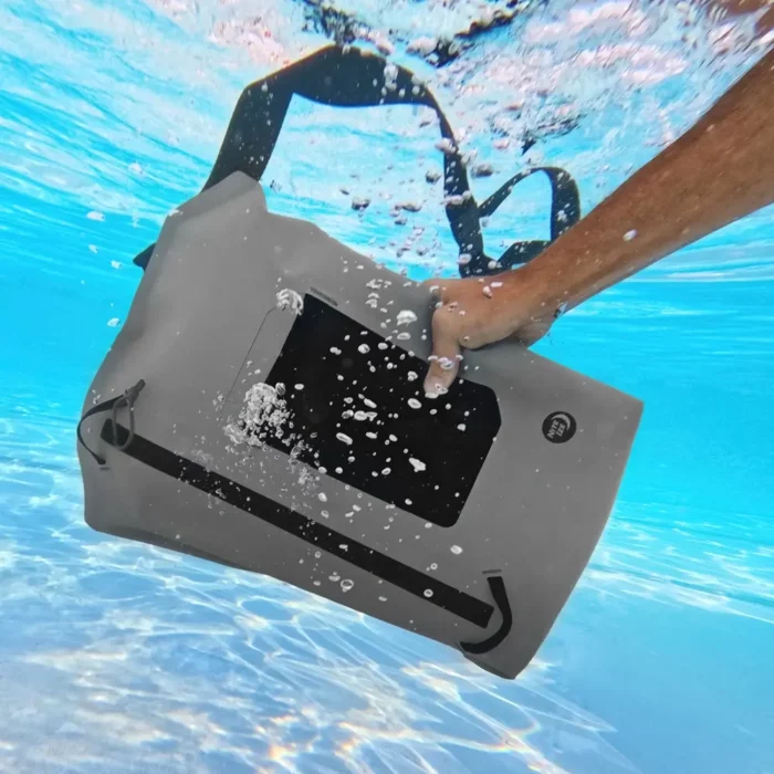Eine Hand taucht eine robuste, graue Tasche vollständig unter Wasser – der wasserdichte Rucksack trotzt den Fluten und schützt den Inhalt zuverlässig selbst bei vollständigem Eintauchen.