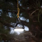 Eine leuchtende Solar Campinglampe hängt abends an einem Seil in einem Baum und sorgt für stimmungsvolle Beleuchtung im Freien.