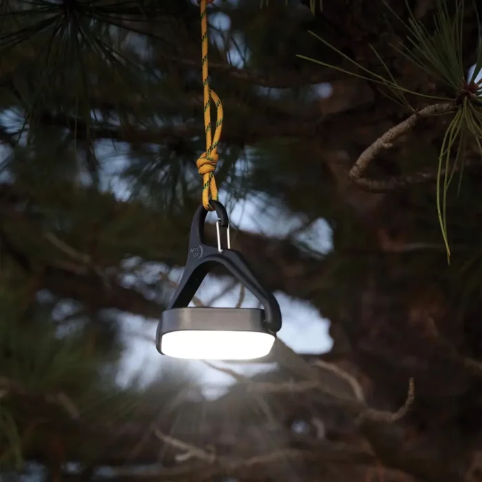 Eine leuchtende Solar Campinglampe hängt abends an einem Seil in einem Baum und sorgt für stimmungsvolle Beleuchtung im Freien.