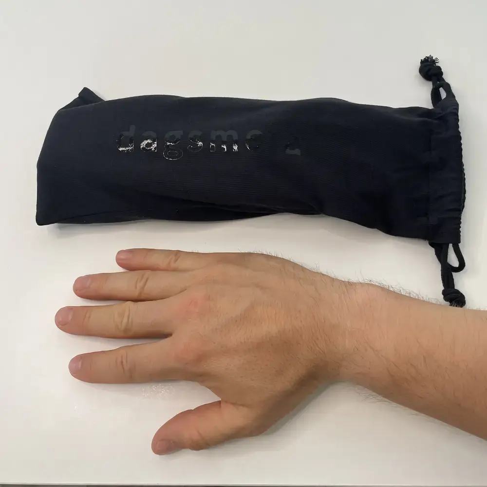 Vergleichsgröße mit Tasche: Schwarzer Aufbewahrungsbeutel der Dagsmejan Blackout Schlafmaske neben einer ausgestreckten Hand zur Größeneinschätzung.