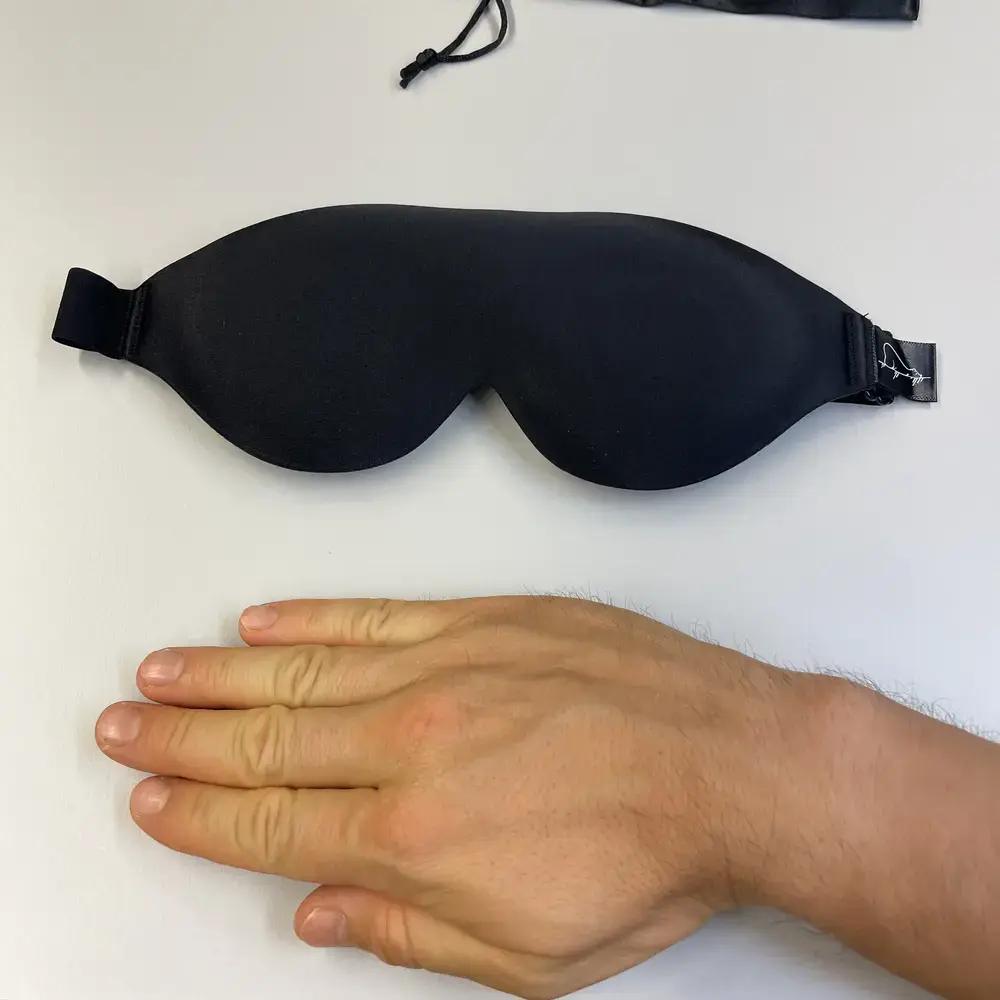 LASKA BEAR 3D Schlafmaske auf weißem Tisch, daneben eine Hand zur Grösseneinschätzung.