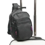 Schwarzes Sling Pack mit pinken Reissverschlussdetails auf dem Griff eines Trolleys befestigt, vor weissem Hintergrund fotografiert.