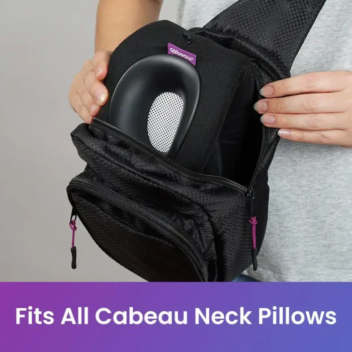 Person verstaut ein schwarzes Cabeau Nackenkissen im Hauptfach eines offenen Sling Packs mit pinken Reissverschlüssen. Unten steht: „Fits All Cabeau Neck Pillows“.