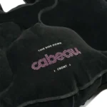 Detailaufnahme eines schwarzen aufblasbaren Sitzkissens mit der Aufschrift „cabeau – this side down – front“ in weiss und pink.