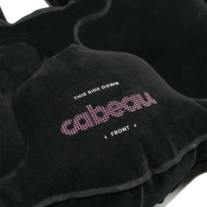Detailaufnahme eines schwarzen aufblasbaren Sitzkissens mit der Aufschrift „cabeau – this side down – front“ in weiss und pink.