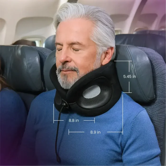 Mann mit grauen Haaren sitzt entspannt im Flugzeugsitz und trägt ein schwarzes Reise Nackenkissen mit seitlichen Belüftungsöffnungen. Masse des Kissens sind eingeblendet: 5.45 in Höhe, 8.8 in Breite und 8.9 in Tiefe.