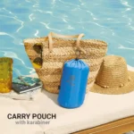Blaues Strandkissen von Go Travel im Kompressionsbeutel mit Karabiner, platziert vor einer geflochtenen Strandtasche am Pool.