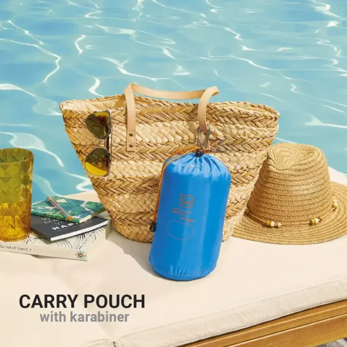 Blaues Strandkissen von Go Travel im Kompressionsbeutel mit Karabiner, platziert vor einer geflochtenen Strandtasche am Pool.