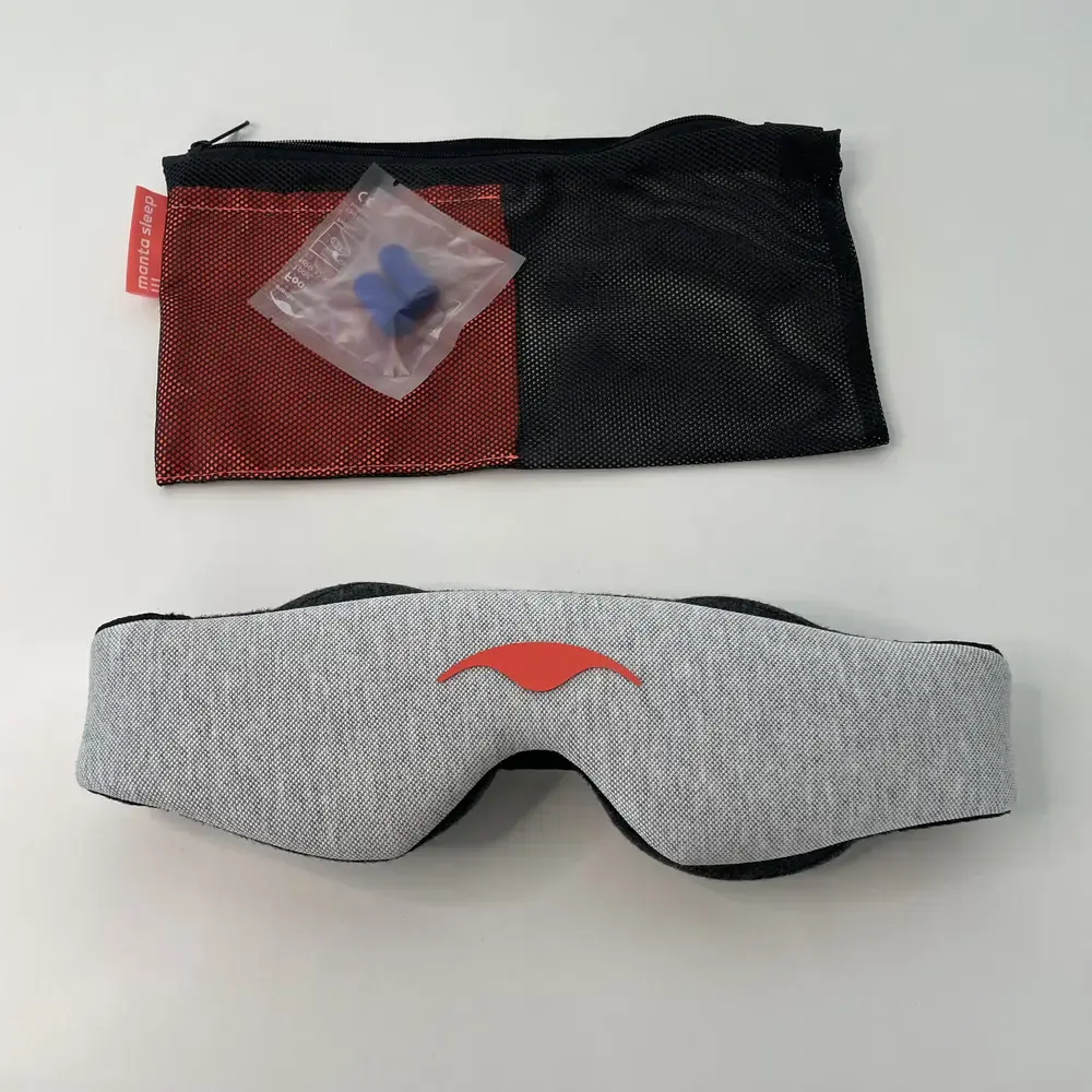 Manta Schlafmaske mit Ohrstöpseln und Transportbeutel auf einem weissen Tisch arrangiert